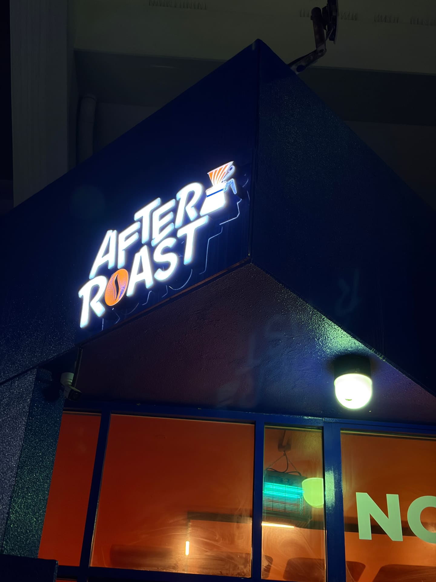 The illuminated AFTER ROAST sign glowing white and orange on the dark blue corner of the building at night.